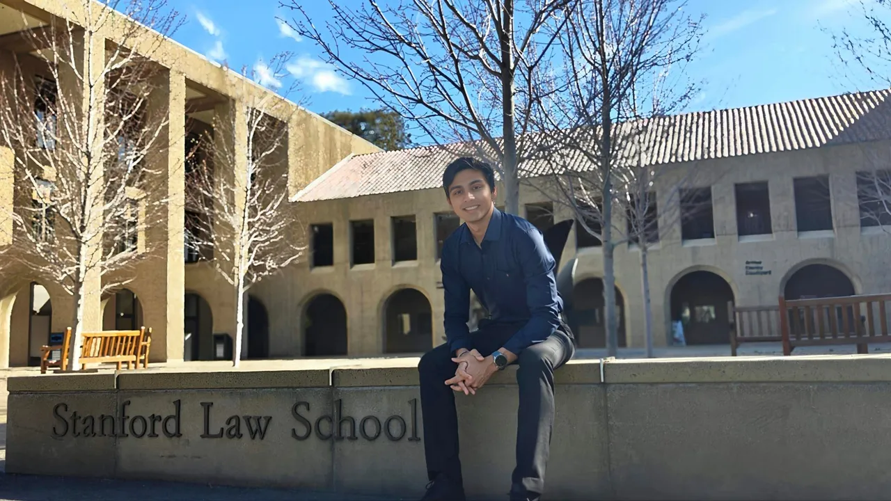 Naman sitting on the Stanford Law School sign